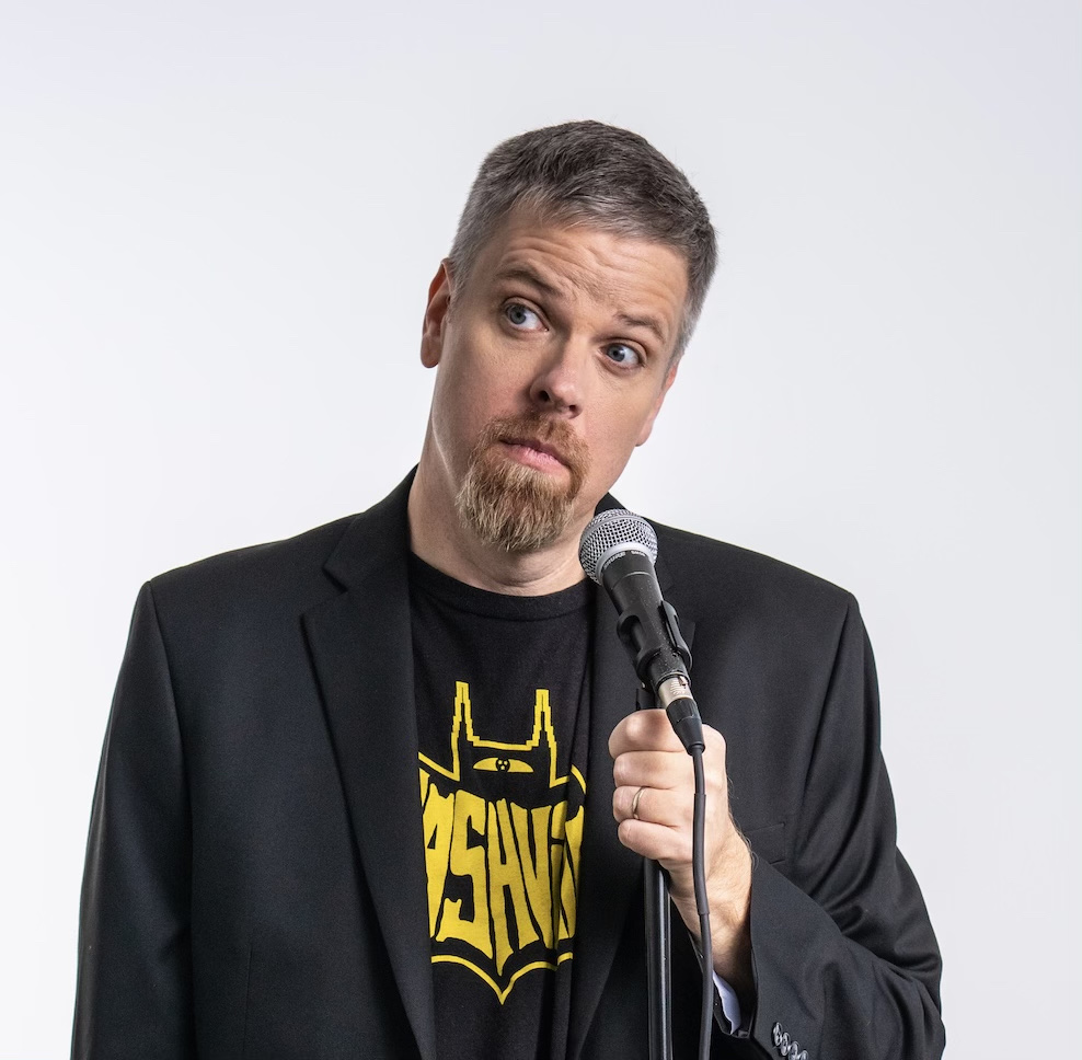 Jonnie W. holding a microphone, giving the camera a skeptical look