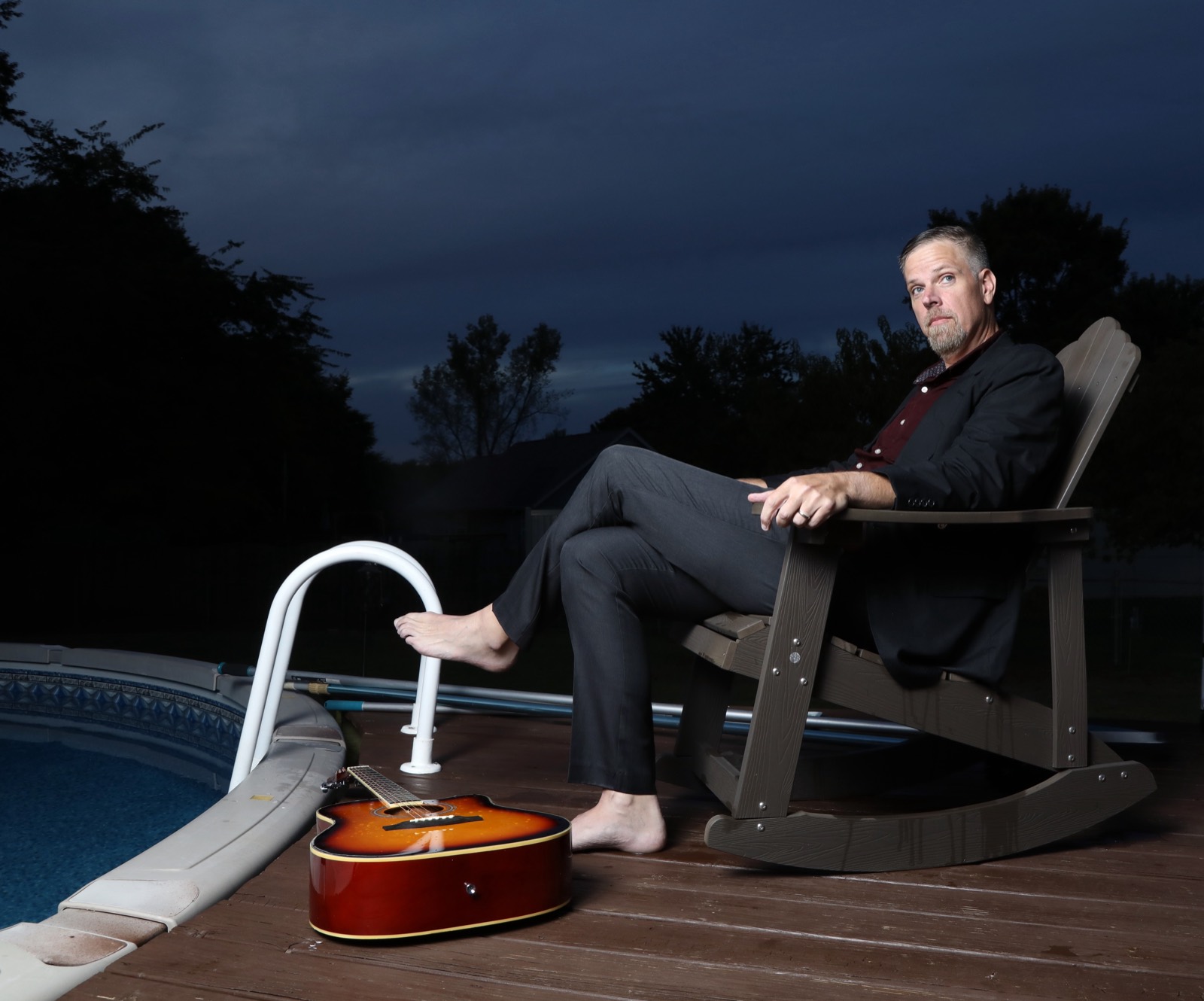 Jonnie W. in a rocking chair beside a pool, guitar at his feet